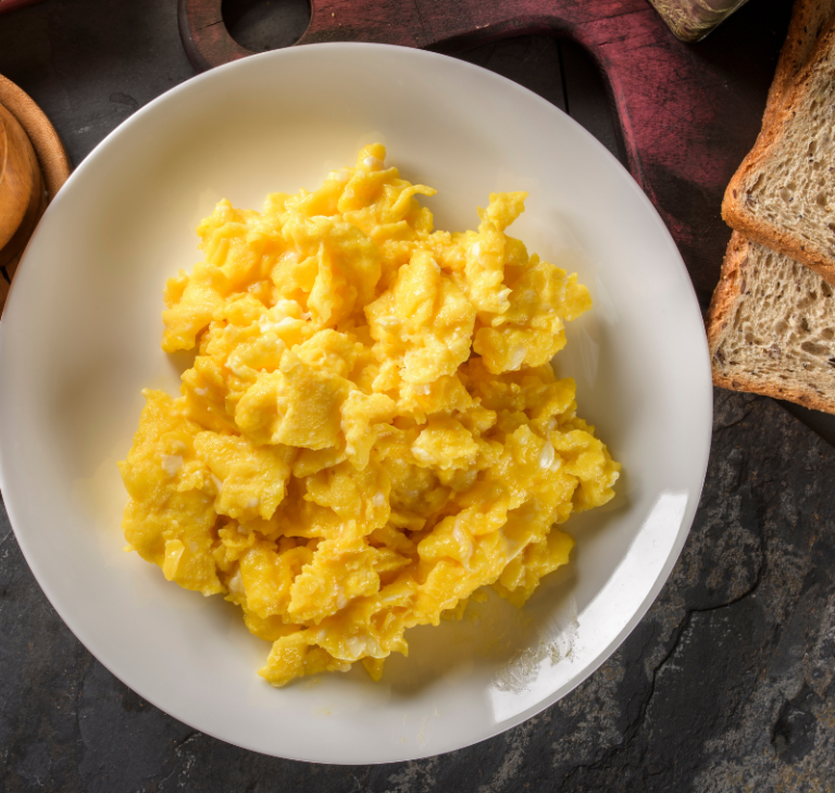 Plate of soft, fluffy scrambled eggs served with buttered toast, milk, and melted butter on a wooden table