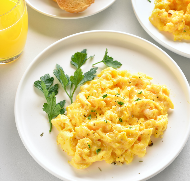 Plate of soft, fluffy scrambled eggs served with buttered toast, milk, and melted butter on a wooden table